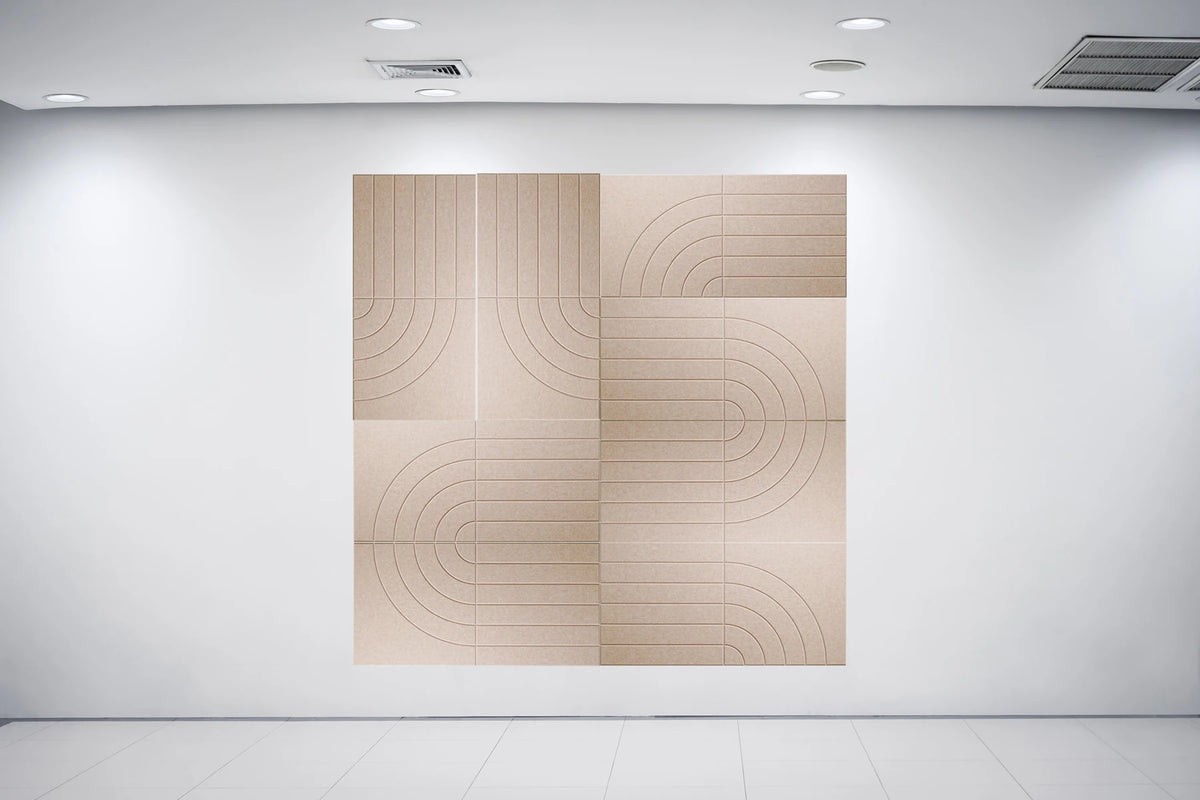 A large square wall art piece with a beige and light brown geometric pattern of concentric arches and lines, displayed on a white gallery wall under ceiling spotlights.