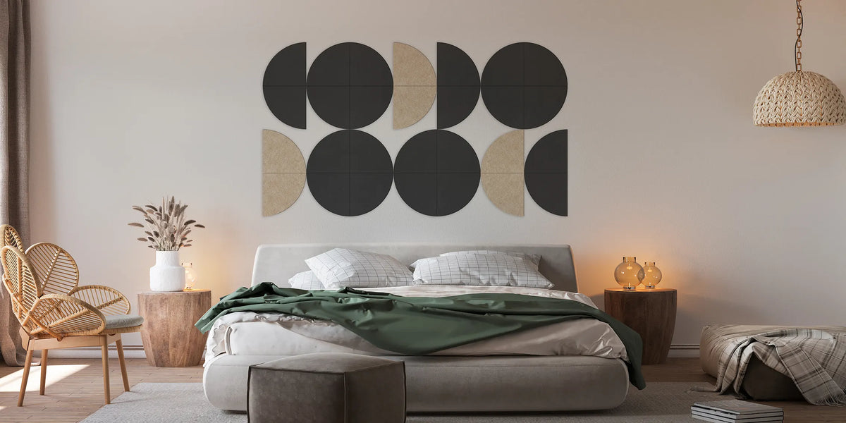 A modern bedroom interior with a bed, side tables, chair, pendant light, and a large geometric wall art piece above the bed. The wall art consists of black and beige circular and semicircular shapes on a light beige wall.