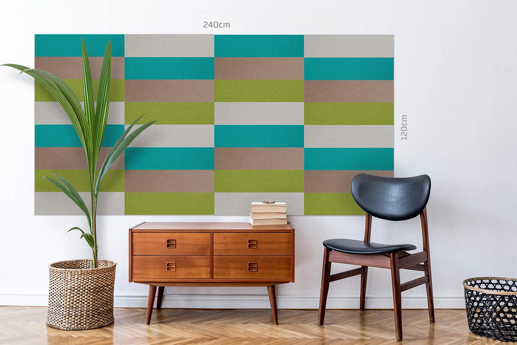 A large geometric wall mural or wallpaper sample with repeating rectangular blocks in teal, olive green, tan, and light gray, shown installed on a white wall in a styled room with a plant, mid-century sideboard, chair, and basket.