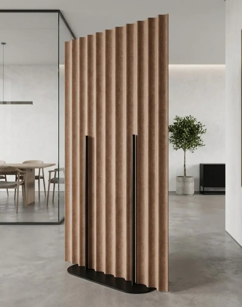 A modern slatted privacy screen divider in a warm tan or light brown textured material, mounted on a sleek black metal base inside a contemporary minimalist office or living space.