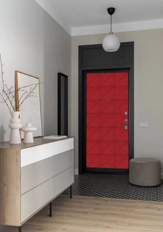 A modern interior entryway featuring a bold red geometric-patterned front door with a black frame, styled with a light wood and white credenza, white ceramic vases, a gray pouf, and a black-and-white patterned rug.