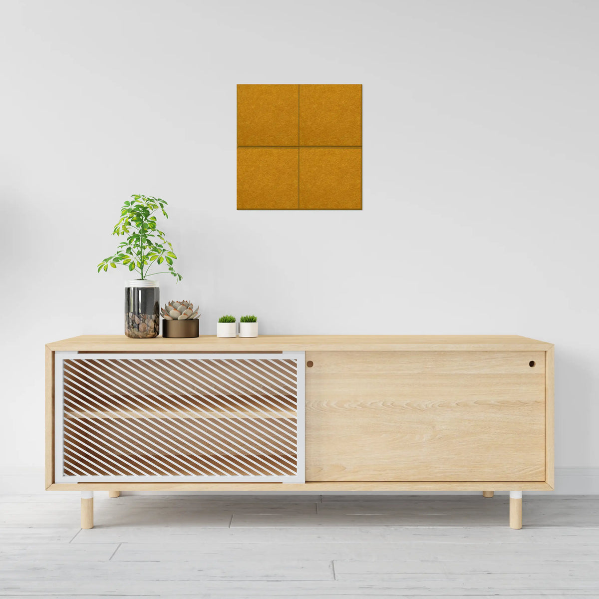 A modern light wood sideboard cabinet with a slatted front panel and a solid wood door, styled in a minimalist room setting with a plant and small pots on top, and a square orange wall art piece above.
