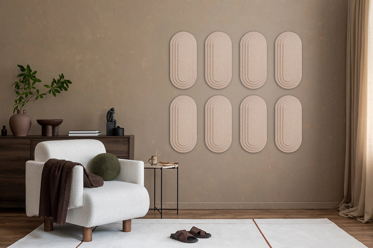 A styled interior room with a beige wall featuring eight ribbed oval wall panels arranged in two rows. A white armchair with a brown throw blanket, a small side table, a plant, and a rug are visible in the room.