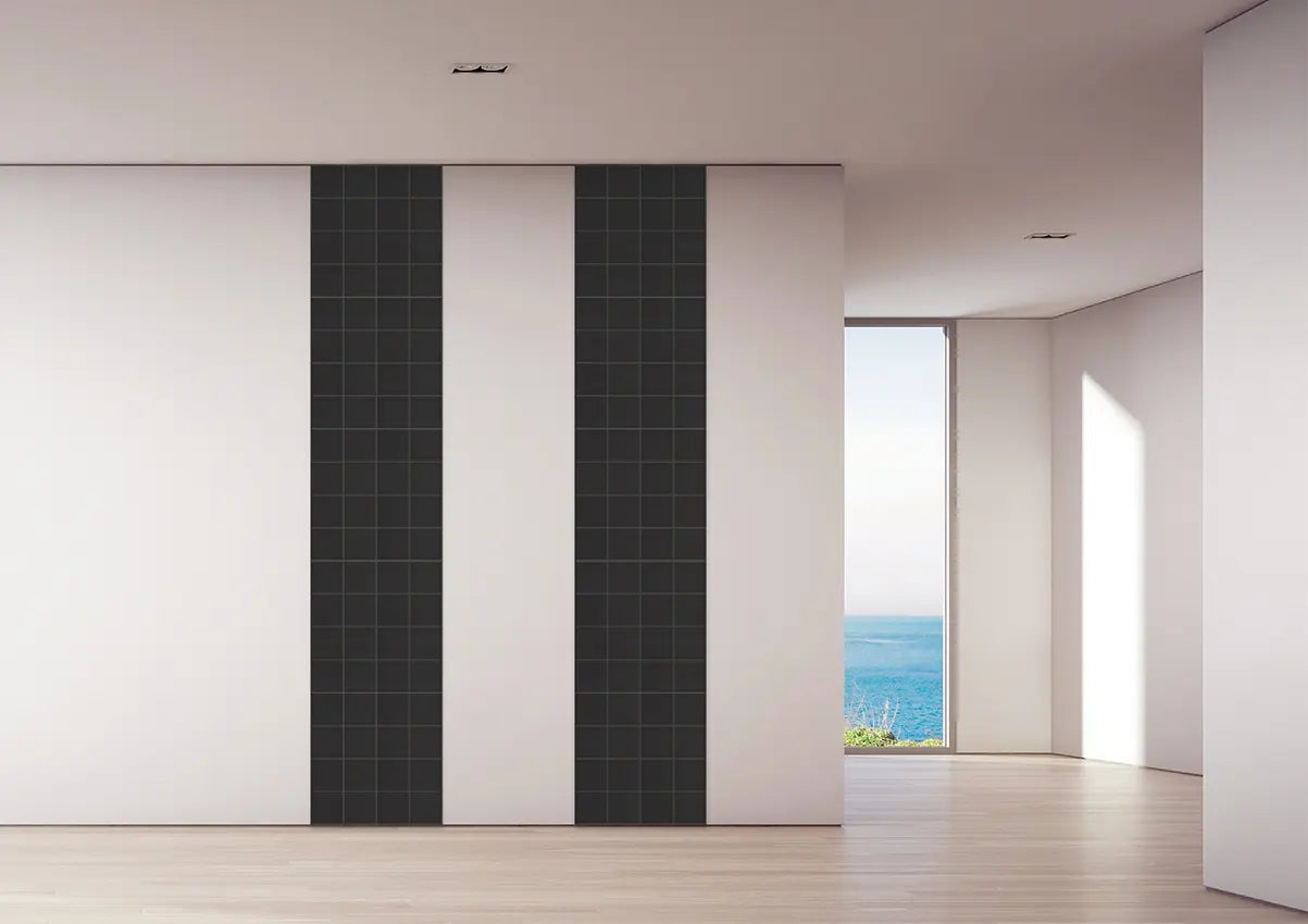 Modern interior wall paneling featuring two tall vertical black grid-patterned panels flanked by white panels, set in a minimalist room with light wood floors and a window looking out to the ocean.