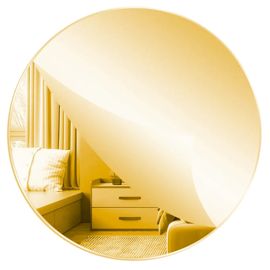 A circular mirror with a reflective gold-toned frame, showing a warm yellow-gold interior scene with a window seat, curtains, drawers, and a chair. The mirror is centered on a plain white background.