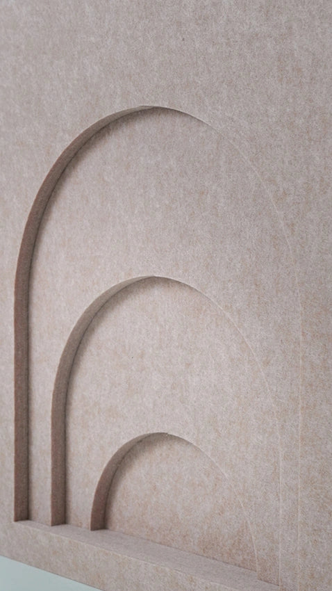 A close-up of a textured beige surface with three nested arch recesses in a slightly darker taupe tone.