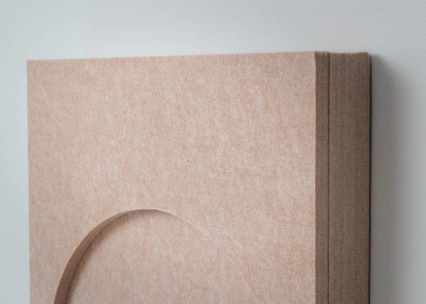 A close-up of a textured beige wall art panel with a curved recessed detail and layered side edges, shown against a light gray wall.