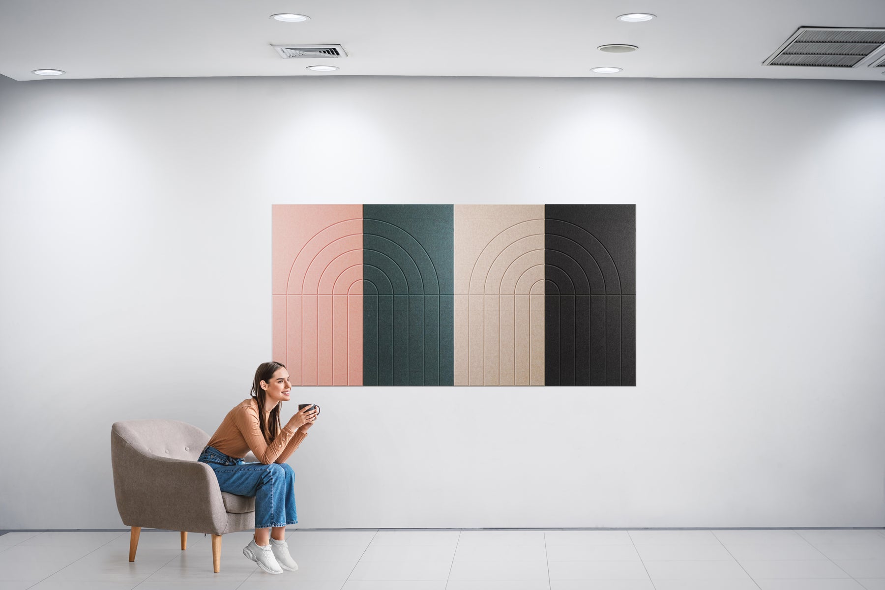 A person seated in a chair against a wall, with a large Art Deco style painting hanging on the wall behind them. The painting features geometric shapes in shades of green, pink, and black.
