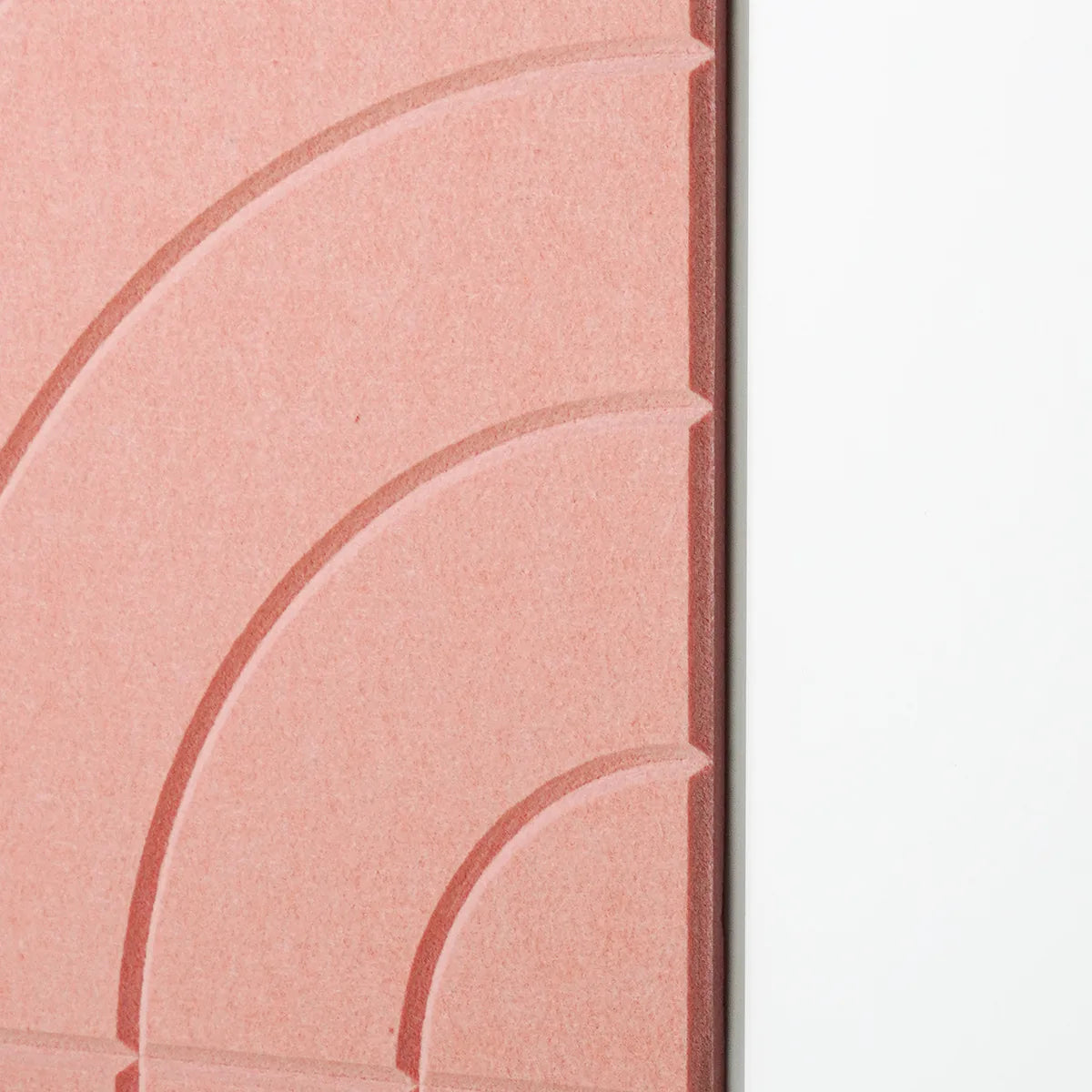 A close-up of a textured pink panel with embossed concentric arch patterns, positioned next to a plain white surface.