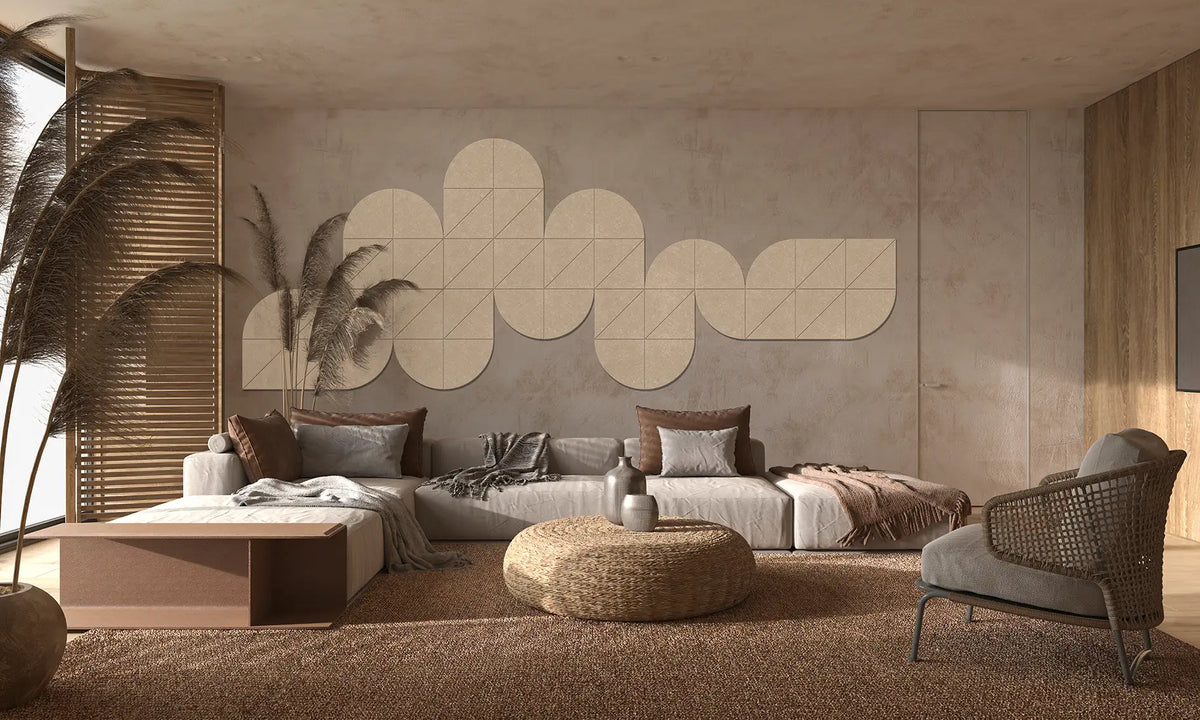 A modern living room interior with a low beige sectional sofa, neutral-toned cushions, a round woven ottoman, a gray armchair, and a large geometric wall art piece mounted on the back wall.