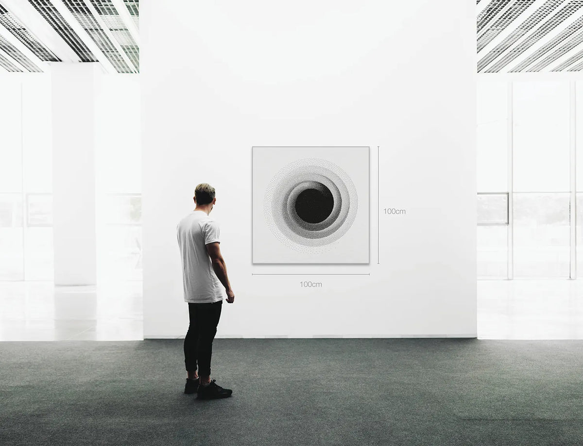 A man stands in a bright modern gallery space facing a large square wall art piece with concentric circular design. The artwork is shown in perspective with dimension labels reading 100cm by 100cm on the wall.