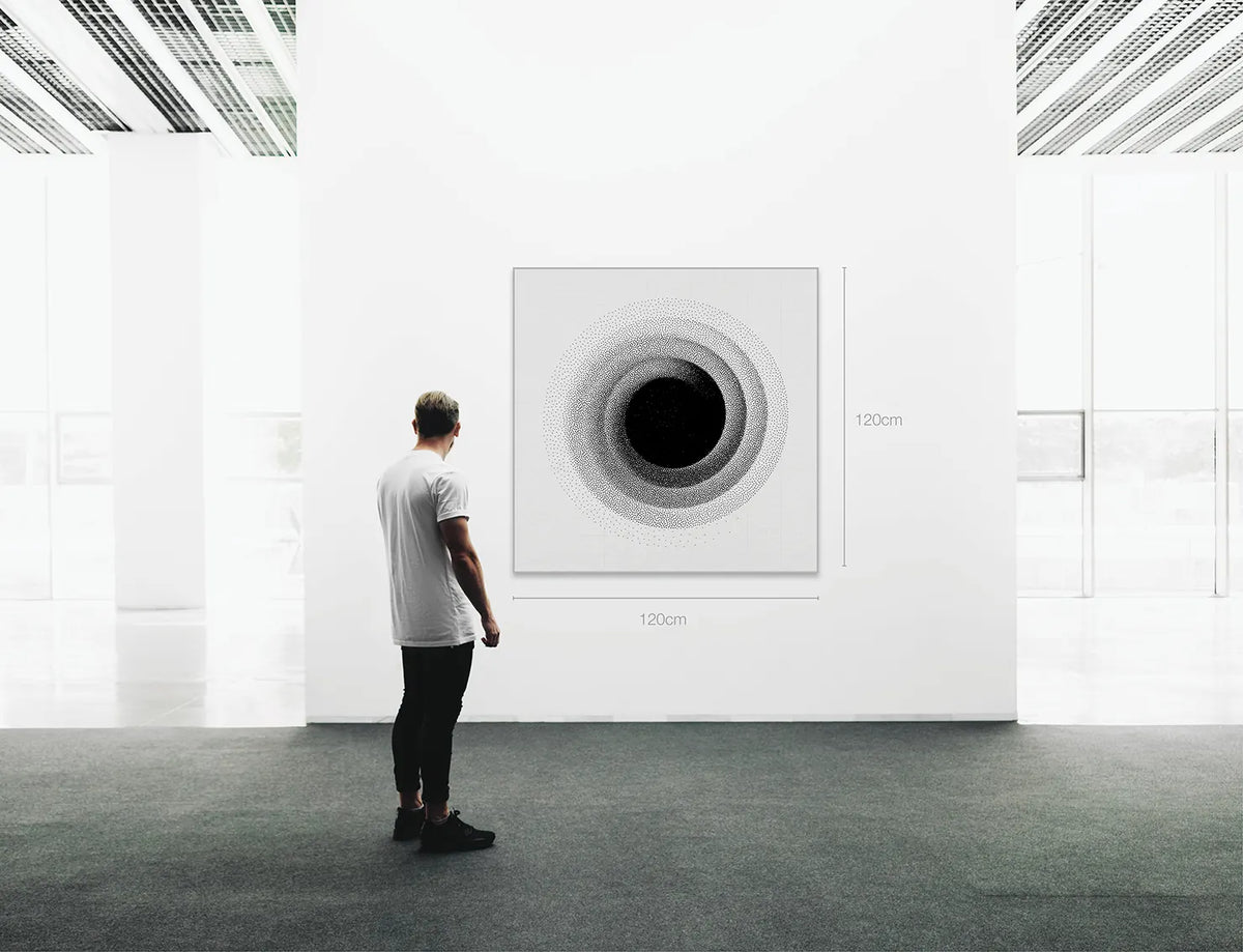 A man stands in a bright white gallery space facing a large square wall art print with a circular black-and-gray spiral design. Small dimension labels reading 120 cm × 120 cm are visible near the print.
