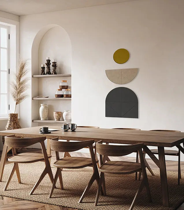 A modern dining room scene featuring a long wooden dining table and matching wooden chairs arranged on a woven rug. The room has warm off-white walls with built-in shelves, decorative vases, and wall art in yellow, beige, and charcoal.