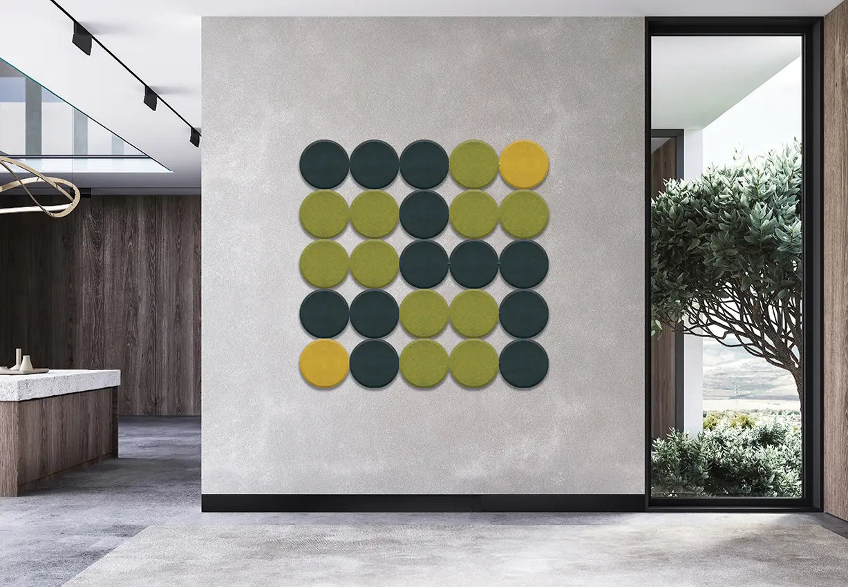 A modern wall-mounted circular art piece featuring a grid of 24 textured circles in dark green, olive green, and mustard yellow, displayed on a concrete-textured wall in a contemporary interior setting.