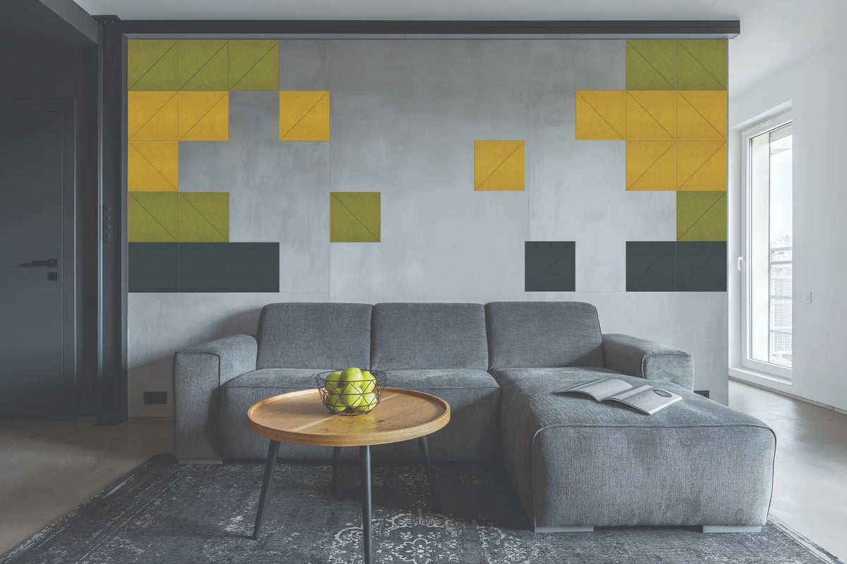 A modern living room featuring a large geometric wall mural with yellow, olive green, and dark gray blocks on a textured gray background, positioned above a gray sectional sofa.
