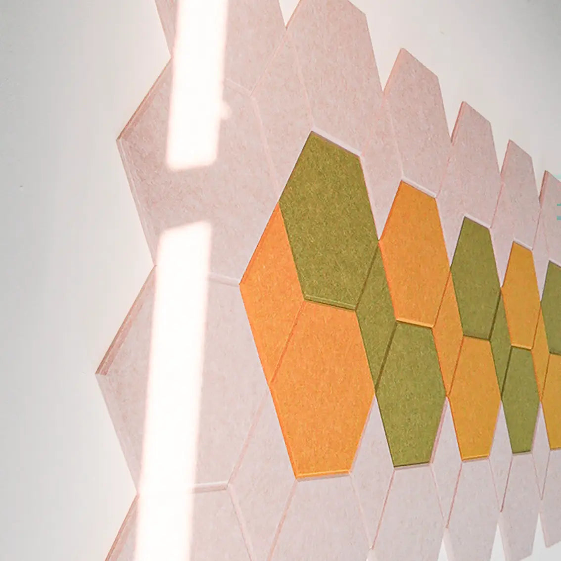 Hexagonal wall tiles in orange and olive green arranged in a zigzag pattern on a white wall, with a bright light reflection running vertically.