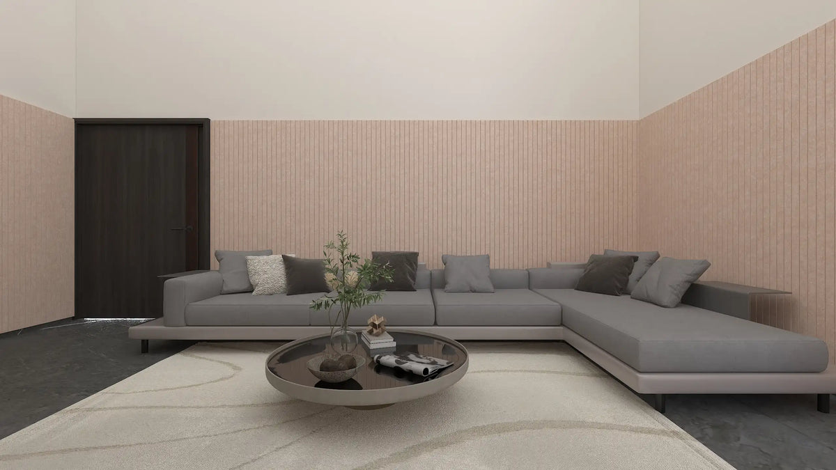 A modern L-shaped gray sectional sofa with dark gray and white throw pillows, set in a minimalist living room with a light beige rug, a round coffee table, and pink textured accent walls.