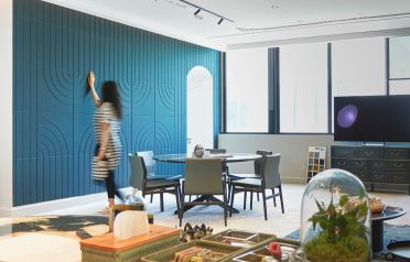 A woman in a striped dress walks past a large blue accent wall with arched panel details in a modern dining room setting.
