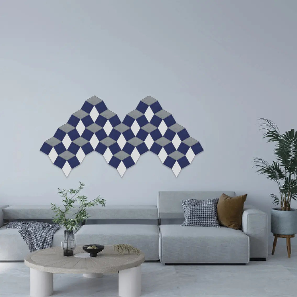 A modern living room setting featuring a geometric wall art piece made of interlocking 3D diamond blocks in navy blue, gray, and white, mounted on a light gray wall above a light gray sectional sofa.