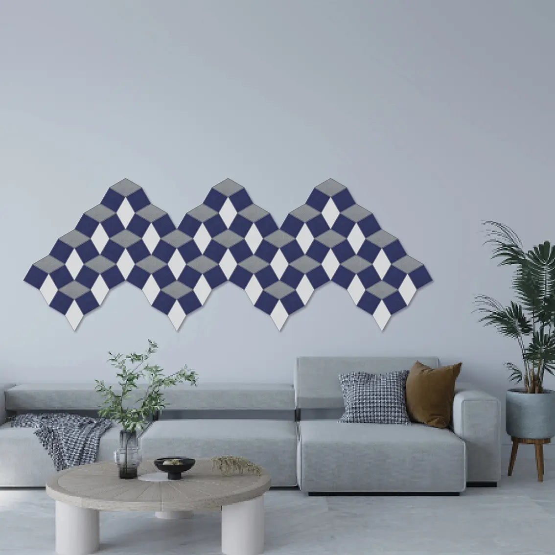 A modern living room setting featuring a decorative wall art piece made of repeating 3D-effect diamond shapes in navy blue, gray, and white, mounted on a light gray wall above a light gray sectional sofa.
