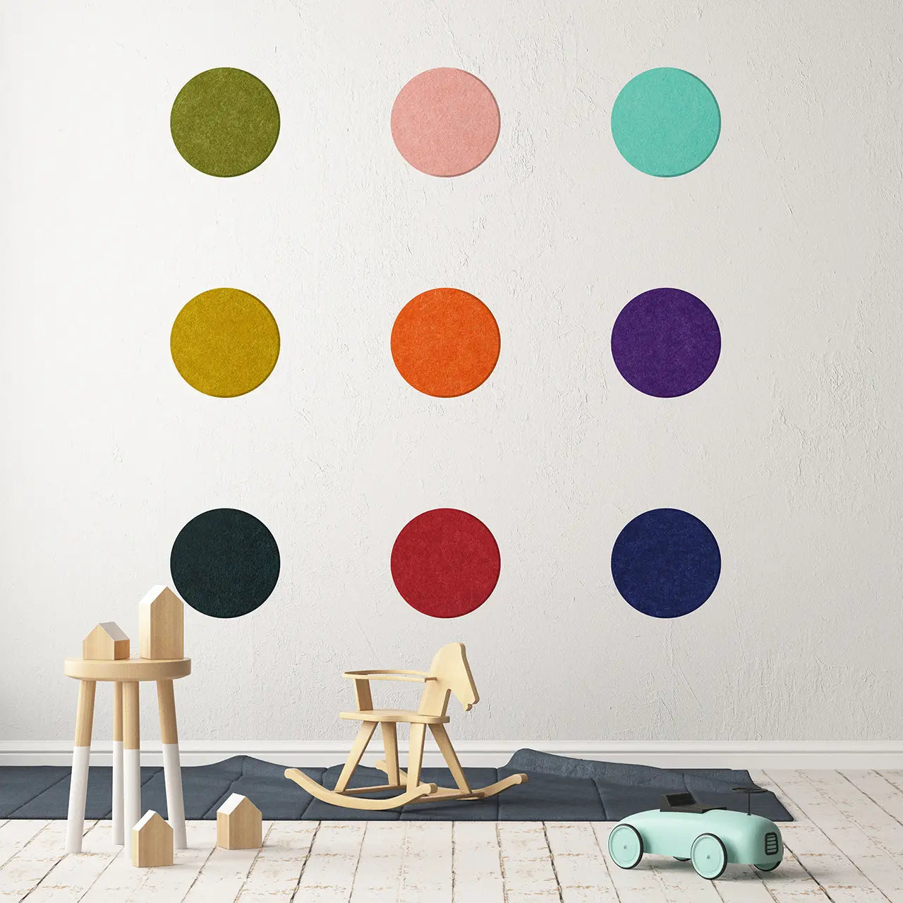 A wall adorned with multicolored circular polka dot panels in various sizes, with a wooden rocking horse and toy car on the floor in front of it.