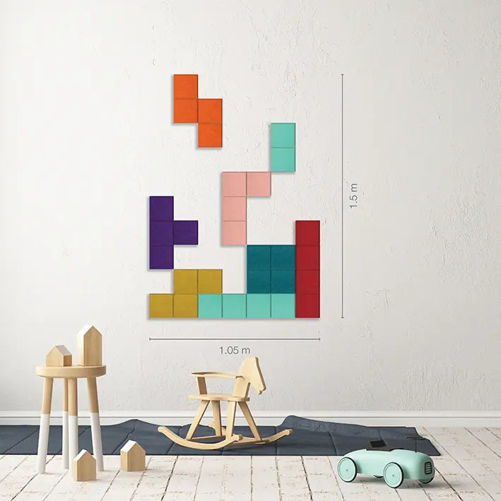 A colorful wall-mounted block puzzle art piece displayed on a white wall in a styled children's room, with wooden toys and a rocking chair below. Measurement lines and labels indicate the dimensions of the wall art.