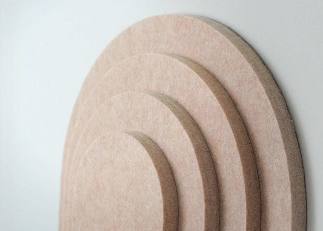 A close-up of a set of concentric semi-circular beige felt pads or mats against a plain light background.