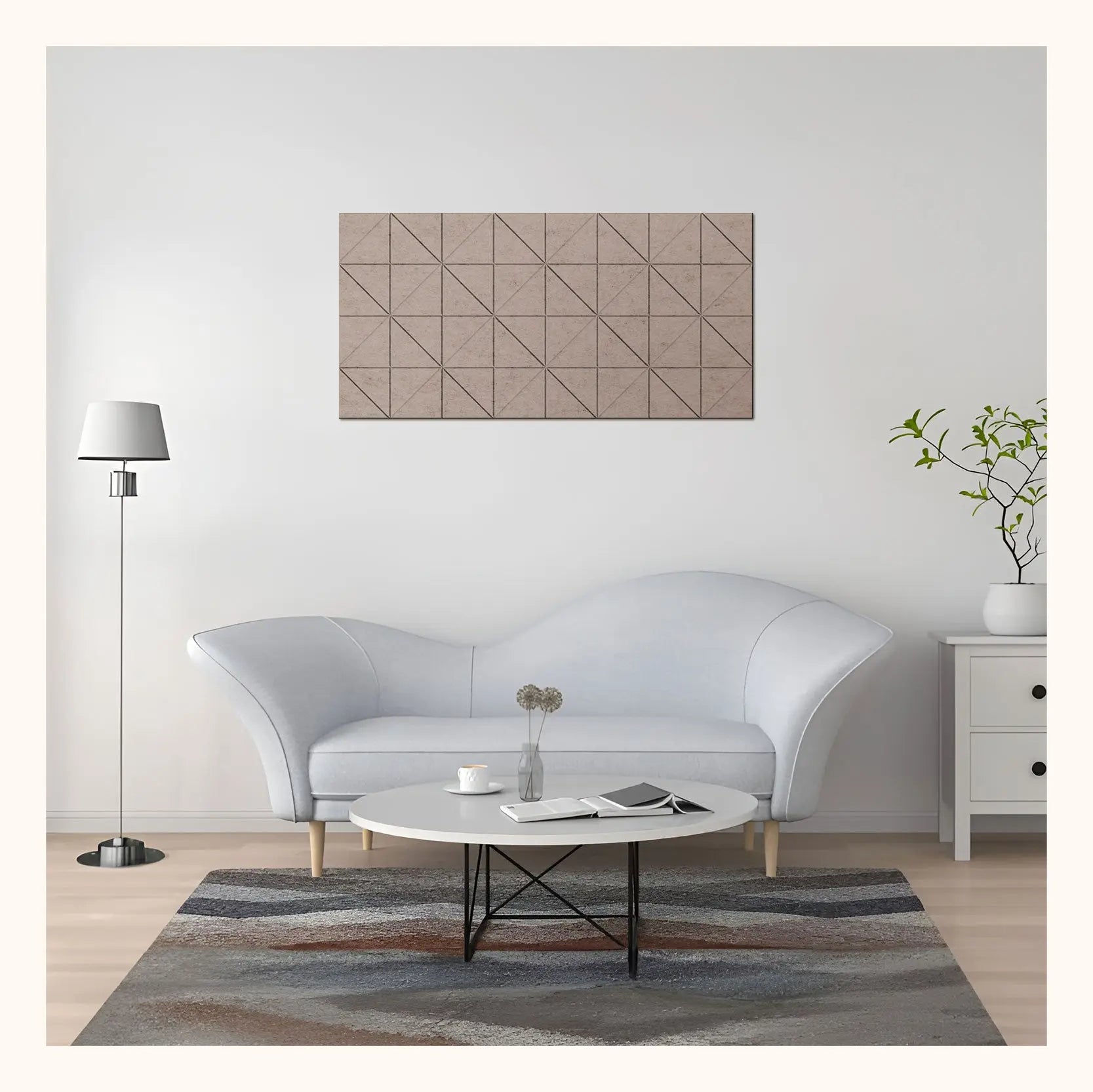 A modern living room scene featuring a rectangular wall art piece with a geometric triangular pattern in beige and brown tones, hung above a light gray curved sofa.