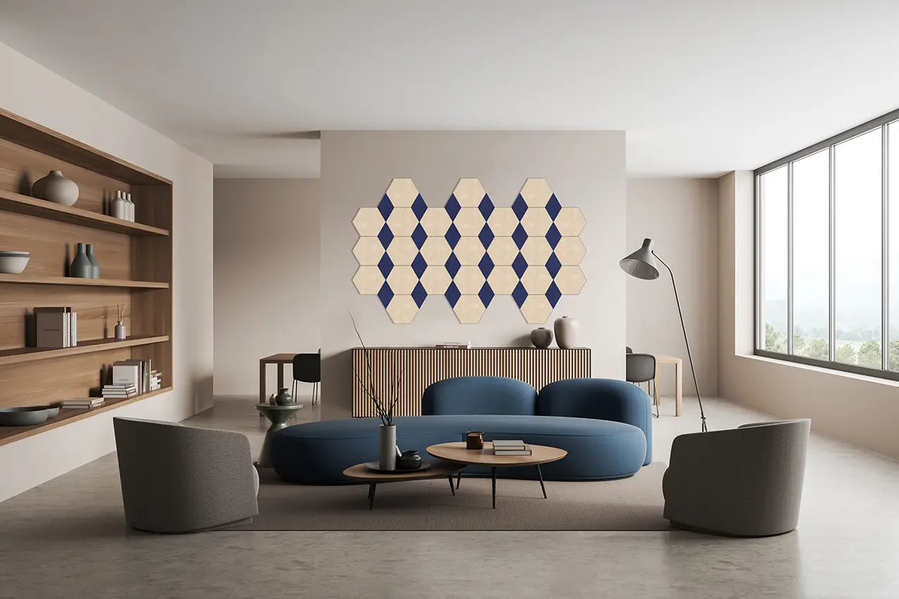 A modern living room interior featuring a curved blue sofa, gray armchairs, round wooden coffee tables, a tall floor lamp, built-in wooden shelving, and a geometric hexagon wall art piece in blue and cream mounted on the back wall.