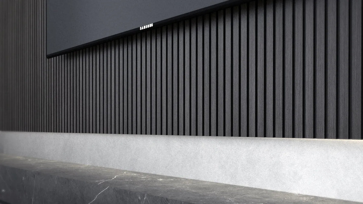 A close-up of a modern wall paneling system featuring dark charcoal gray vertical slats with a textured light gray concrete base and a dark stone countertop.